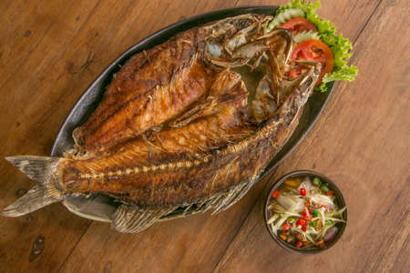 Deep fried whole fish crispy and delicious spicy sauce on a wood table - asian cuisineの写真素材