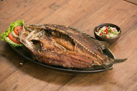 Deep fried whole fish crispy and delicious spicy sauce on a wood table - asian cuisineの写真素材