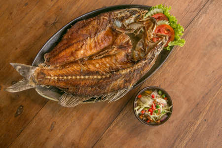 Deep fried whole fish crispy and delicious spicy sauce on a wood table - asian cuisineの写真素材