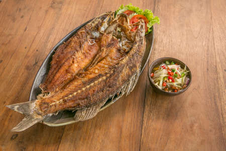 Deep fried whole fish crispy and delicious spicy sauce on a wood table - asian cuisineの写真素材