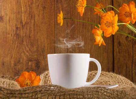 Cup of coffee with orange flowers on wooden backgroundの写真素材