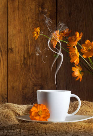 Cup of coffee with orange flowers on wooden backgroundの写真素材