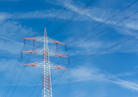 Angled view of a red and white electricity pylon with a blue sky background.の写真素材