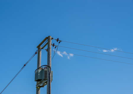 A electricity transformer on two wooden telegraph poles with a blue sky background.の写真素材