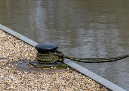 Rope tied to a black mooring bollard on the dock with water in the background.の写真素材