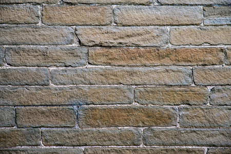 Yellow and grey stone wall with uneven sized brick work and white mortar.の写真素材
