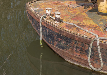 A rusting barge moored by rope with capstans and dark water.の写真素材