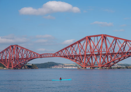South Queensferry, Edinburgh, Scotland 7th September 2021 - A small blue Kayak passing under the Forth Bridge on a sunny day with clear sky.のeditorial素材