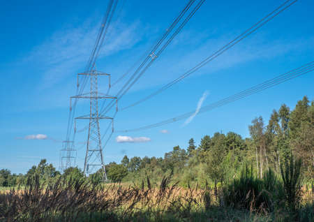 High voltage powerlines with pylons across a blue sky background on a sunny day