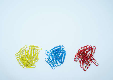 Multi coloured, blue, red and yellow paper clips in piles on a plain white background.の写真素材