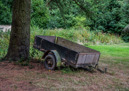Old abandoned trailer next to a tree with over grown grass.