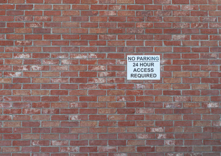 27 January 2022 - A black and white warning sign for no parking and 24 hour access attached to a red brick wall.のeditorial素材
