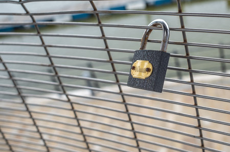 Single grey padlock on a wire mesh fence with gold lable with out of focus background.の写真素材