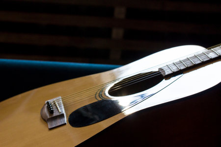 the guitar is acoustic, six-stringed, made of light wood under the rays of the sun on a blue sofa....