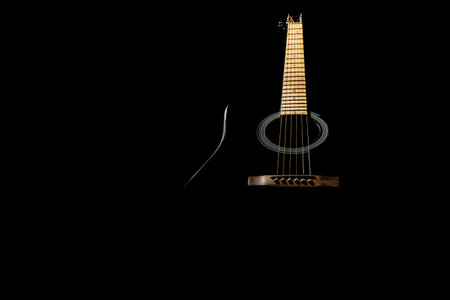 the guitar is black acoustic on a black background, silhouette. close-up, front view from below