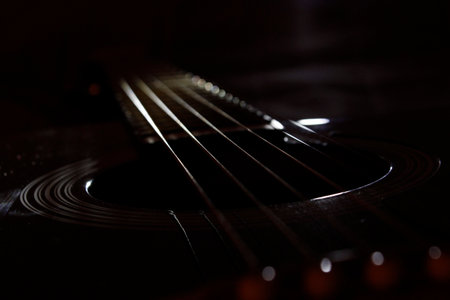 The strings of a six-string guitar shine in the dark. close-up photo in a dark key