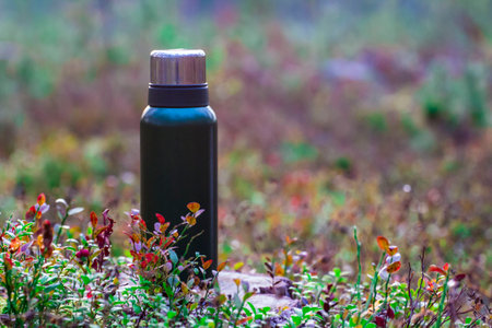 a thermos with a hot drink. hot tea. hot coffee. thermos flask on the background of wild nature. forest background. space for the text. close-up.の写真素材