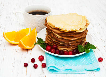 plate with pancakes with cranberries on a wooden background