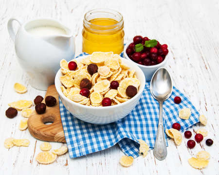 cornflakes with milk, cranberries and nuts on a wooden tableの写真素材