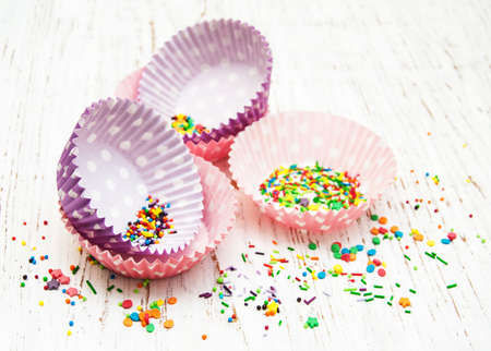 empty cupcake cups and color sprinkles on a old wooden backgroundの写真素材