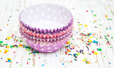 empty cupcake cups and color sprinkles on a old wooden backgroundの写真素材