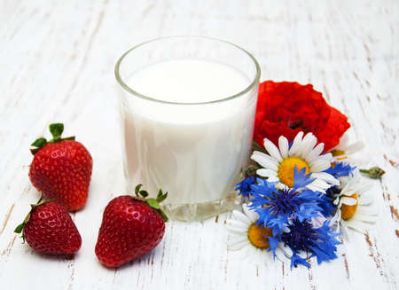Glass of milk with strawberry and wildflowers on a old wooden backgroundの写真素材