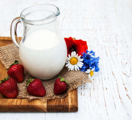 Jug of milk, strawberries and wildflowers on a old wooden backgroundの写真素材