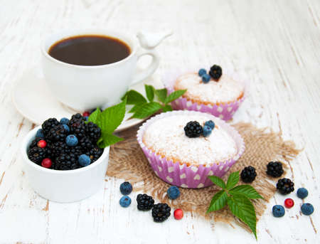 Muffins with fresh berries and cup of coffee on a wooden backgroundの写真素材