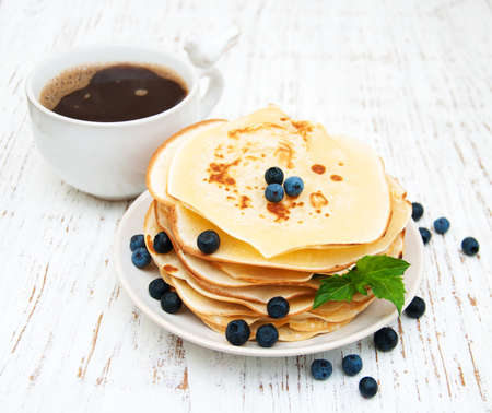 Pancakes with fresh berries, cup of coffee and milk on a wooden tableの写真素材