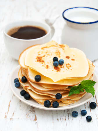 Pancakes with fresh berries, cup of coffee and milk on a wooden table