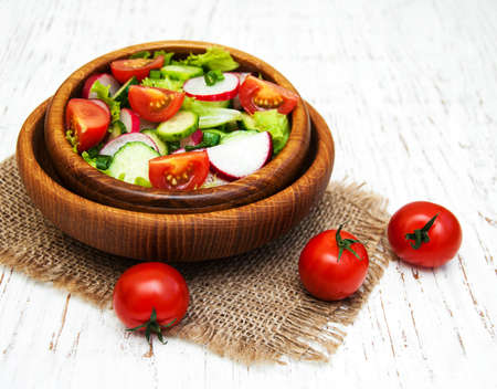 Spring salad with tomato, cucumbers and radish on a wooden backgroundの写真素材