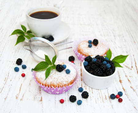 Muffins with fresh berries and cup of coffee on a wooden backgroundの写真素材