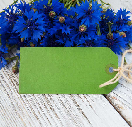 paper tag with blue fresh cornflowers on wooden tableの写真素材