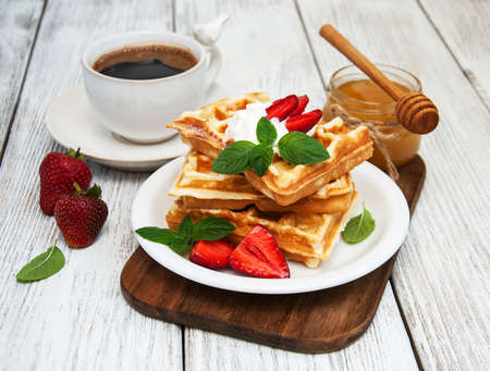 belgian waffles with strawberries and mint with coffee on a wooden tableの写真素材
