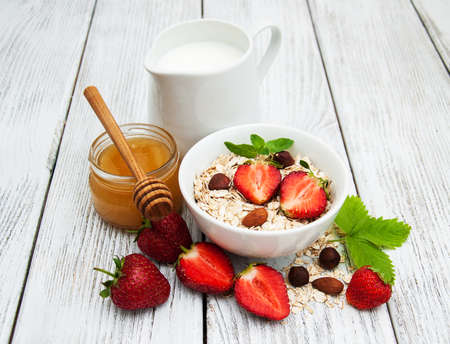 Muesli with strawberries, milk and honey on a old wooden tableの写真素材