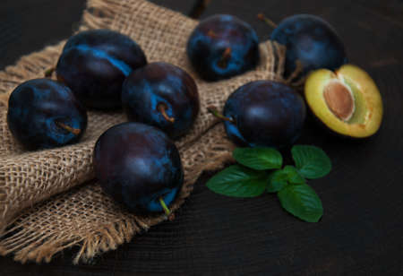 Fresh plums with green leaves on a old black wooden background