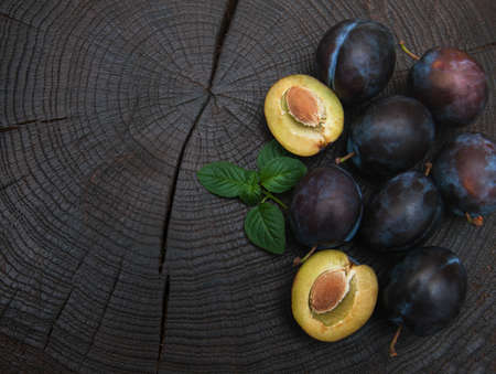 Fresh plums with green leaves on a old black wooden backgroundの写真素材