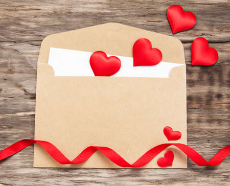 Envelope with red fabric hearts and ribbon on a old wooden background