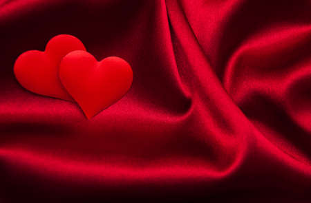 Red hearts on a red silk backgroundの写真素材