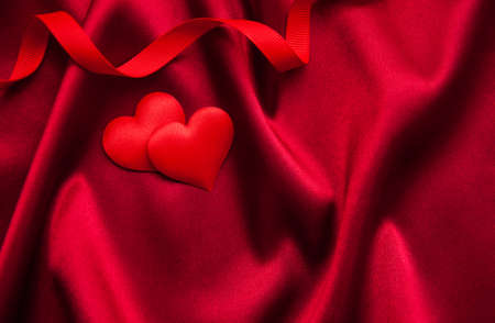 Red hearts on a red silk backgroundの写真素材
