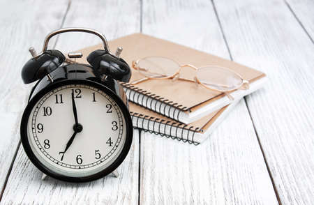 Black alarm clock, notebooks and glasses on a old wooden tableの写真素材