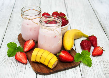 yogurt with fresh strawberries and banana on a old wooden tableの写真素材