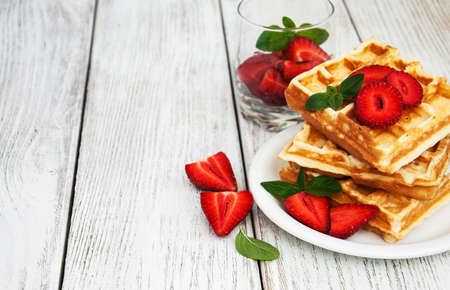 belgian waffles with strawberries and mint with milk on a wooden tableの写真素材