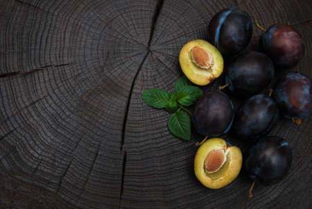 Fresh plums with green leaves on a old black wooden tableの写真素材