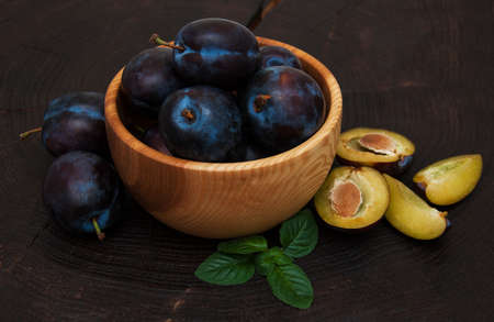 Bowl with  plums with green leaves on a old black wooden backgroundの写真素材