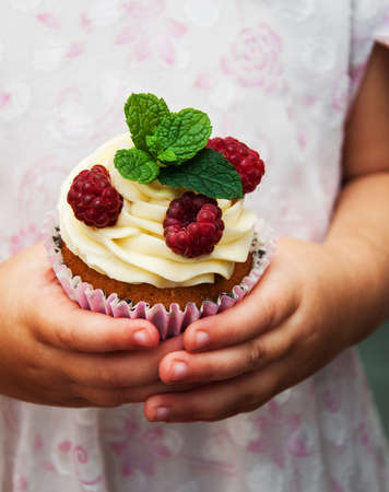 Little girl holding birthday cupcake with raspberriesの写真素材