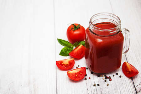 Jars with tomato juice and fresh tomatoes on a tableの写真素材