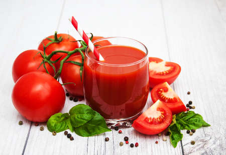 Glass with tomato juice and fresh tomatoes on a tableの写真素材