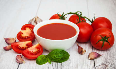 Bowl with tomato sauce and fresh tomatoes on a tableの写真素材