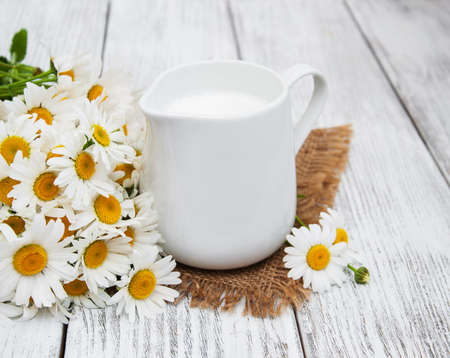 jug with milk  and chamomile flower on a wooden tableの写真素材
